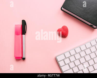 Il giorno di San Valentino concetto laici piana foto Donna di area di lavoro con cuore candy, notebook, marcatori e tastiera su uno sfondo rosa Foto Stock