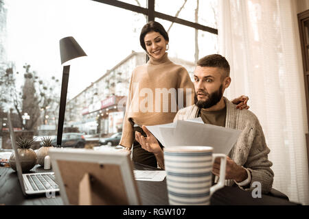 Scioccato barbuto ragazzo che trasportano le carte e mostrando loro a sua moglie Foto Stock