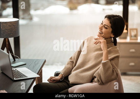 Ridendo donna attraente in colori beige maglione caldo guardando un video Foto Stock