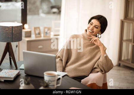 Dai capelli scuri lady attraente seduto alla scrivania e guardare su uno schermo del notebook Foto Stock
