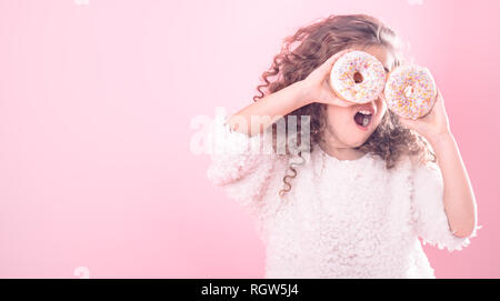 Ritratto di un po' di parentesi ragazza con una bocca aperta e ciambelle nelle sue mani, chiude gli occhi con ciambelle, su uno sfondo rosa, un luogo per il testo Foto Stock