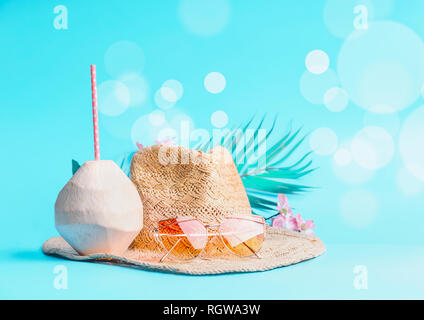 Spiaggia di Womans accessori con cocco fresco, bere cannucce e foglie tropicali e fiori , Occhiali da sole e cappello di paglia sulla soleggiata sfondo blu con Foto Stock