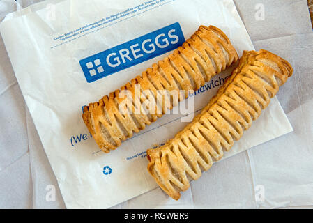 Due Greggs vegano rotoli di salsiccia sul sacchetto di carta con tovaglioli di carta dietro. Foto Stock