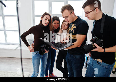 Fotografo spiegare il colpo per il suo team in studio e ricerca sul computer portatile. Parlando con i suoi collaboratori in possesso di una fotocamera durante una foto shoo Foto Stock