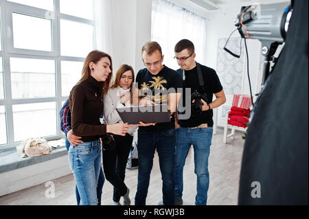 Fotografo spiegare il colpo per il suo team in studio e ricerca sul computer portatile. Parlando con i suoi collaboratori in possesso di una fotocamera durante una foto shoo Foto Stock