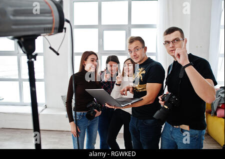 Fotografo spiegare il colpo per il suo team in studio e ricerca sul computer portatile. Parlando con i suoi collaboratori in possesso di una fotocamera durante una foto shoo Foto Stock