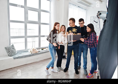 Fotografo spiegare il colpo per il suo team in studio e ricerca sul computer portatile. Parlando con i suoi collaboratori in possesso di una fotocamera durante una foto shoo Foto Stock