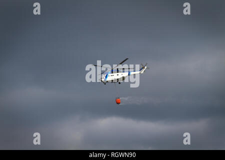 Antincendio con elicottero bambi cesta caricata con acqua sul suo cammino per un incendio Foto Stock