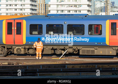 Clapham Junction, UK; 30 gennaio 2019; South Western Railway dipendente in arancione ad alta visibilità abbigliamento di sicurezza sorge nella parte anteriore del treno di passaggio Foto Stock