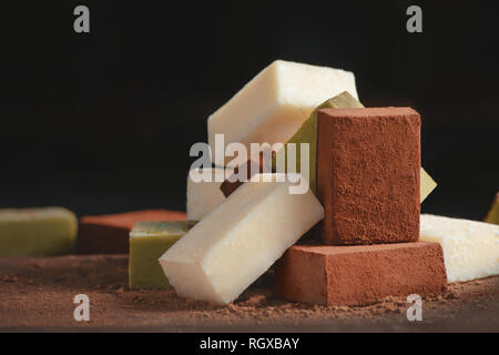 Assortimento di cioccolatini morbido su uno sfondo nero con copia spazio. Latte e matcha giapponese cioccolato gourmet close-up Foto Stock