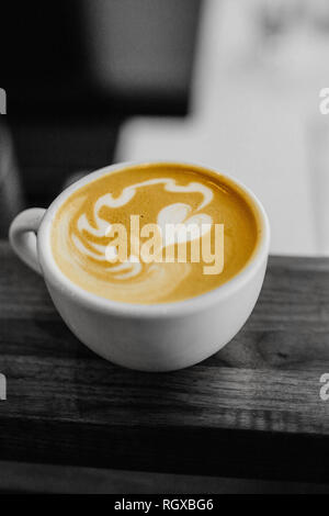 Un bianco tazza di caffè con un cuore schiuma di latte art sulla parte superiore, seduto su un tavolo, in bianco e nero, monocromatiche. Foto Stock