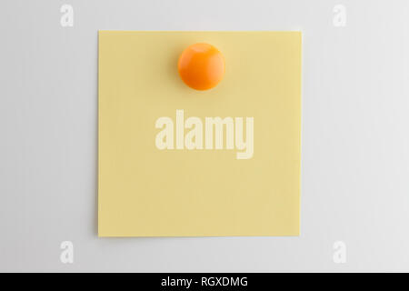 Square foglio di carta gialla imperniati con pulsante arancione magnete sul frigorifero bianco Foto Stock