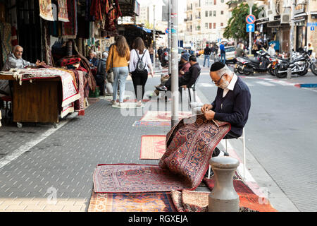 Tel Aviv, Vecchia Jaffa, Israele - 23 dicembre 2018: un vecchio ebreo tappeto venditore la riparazione di un tappeto sulla strada di fronte al suo negozio nel famoso mercato delle pulci, vecchio Foto Stock