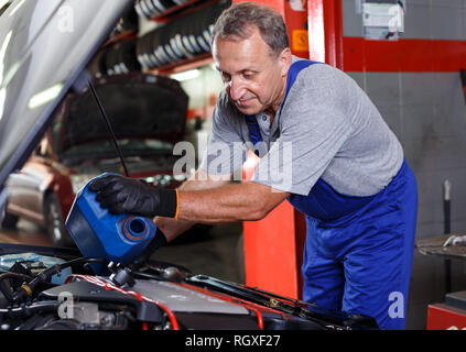 Esperto maturo mechanician auto cambio olio motore nel veicolo in negozio di riparazioni auto Foto Stock