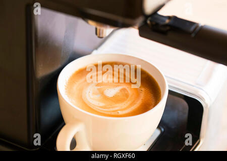 Tazza di cappuccino con crema soffice schiuma di latte, vista dall'alto sulla macchina per caffè , caffè appena fatto Foto Stock