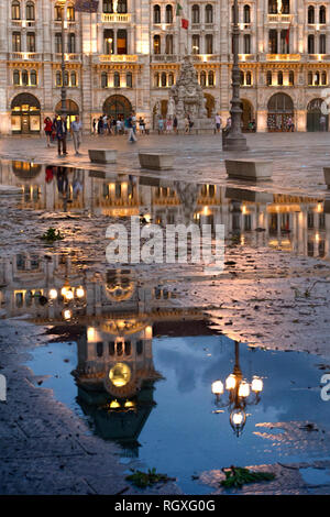 Trieste. L'Italia. Il campanile e la torre dell orologio si riflette in una grande pozza dopo una pioggia pesante. Foto Stock