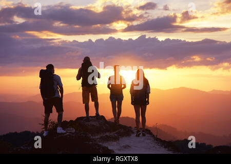 Il gruppo di quattro turisti o amici sorge sulla cima della montagna e guarda al tramonto. I popoli concetto di viaggio Foto Stock