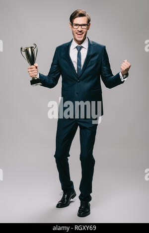 Bello imprenditore celebrando la vittoria e trofeo tenuta in mano su sfondo grigio Foto Stock