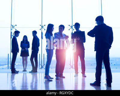 Sagome di asian corporate executives in piedi di fronte a finestre discutere di affari con computer portatile. Foto Stock