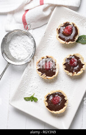 Mousse al cioccolato in pasticceria gusci con lamponi e zucchero a velo. Foto Stock