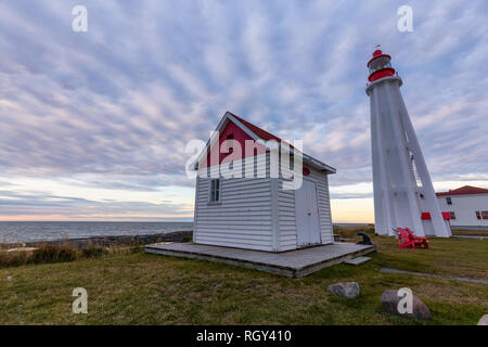 Vista di un faro sulla costa dell'Oceano Atlantico durante un NUVOLOSO TRAMONTO. Tenuto presso lo storico museo marittimo di Rimouski, Quebec, Canada. Foto Stock