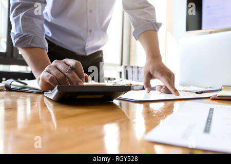 Imprenditore il mani utilizzando una calcolatrice e i dati finanziari analisi sulla scrivania di legno in ufficio Foto Stock
