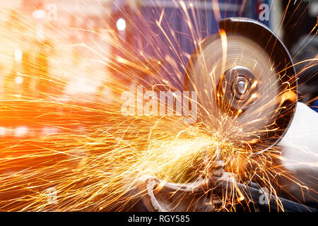 Close-up sui lati volare scintille luminose dall'angolo macchina rettificatrice. Un giovane maschio saldatore in un bianco guanti da lavoro macina un prodotto metallico con angl Foto Stock