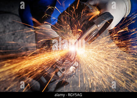 Un close-up di un meccanico utilizzando un metallo smerigliatrice per tagliare una parte di auto in un negozio di riparazioni auto, arancio luminoso lampeggia battenti in direzioni diverse, Foto Stock