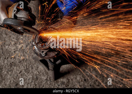 Un close-up di un meccanico utilizzando un metallo smerigliatrice per tagliare una parte di auto in un negozio di riparazioni auto, arancio luminoso lampeggia battenti in direzioni diverse, Foto Stock