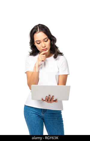 Considerato giovane donna asiatica utilizzando laptop e toccando il mento dal dito isolato su bianco Foto Stock