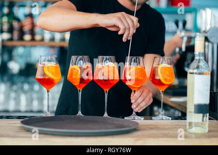 Cinque i cocktail colorati preparati da un barman con pezzi di arancia e cubetti di ghiaccio. Foto Stock