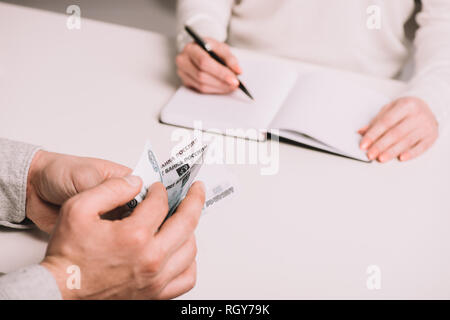 Ritagliato colpo di uomo di rubli di conteggio banconote e la donna la scrittura in notebook Foto Stock