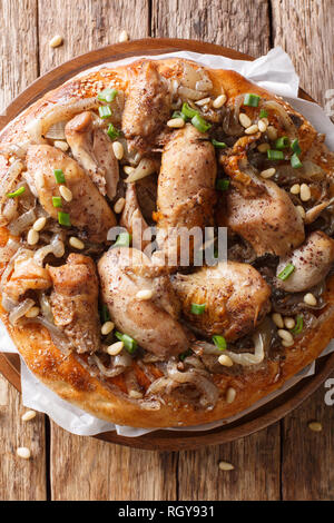 Piatto palestinese di pollo con sommaco, i pinoli e le cipolle su un pane piatto closeup sul tavolo. Verticale in alto vista da sopra Foto Stock