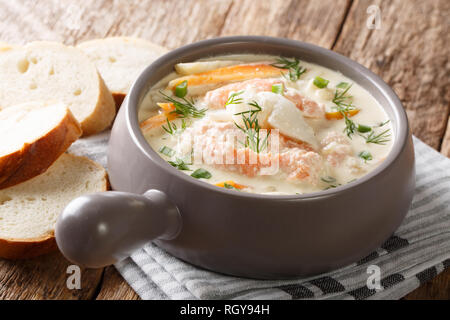 Primo piano della cremosa zuppa di pesce con merluzzo bianco, salmone, la carota e il sedano in una terrina servita con pane fresco sul tavolo orizzontale. Foto Stock