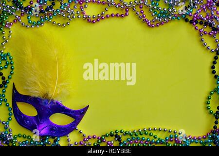 Un giallo Mardi Gras sfondo inquadrato dalla sfera colorata collane con una maschera veneziana in un angolo. Foto Stock