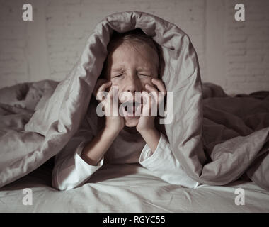 Carino addormentato ragazza urlando e piangendo dopo aver paura o ricalcatura sogno copertura lei stessa con coperta in letto a notte in mood illuminazione drammatica in Foto Stock