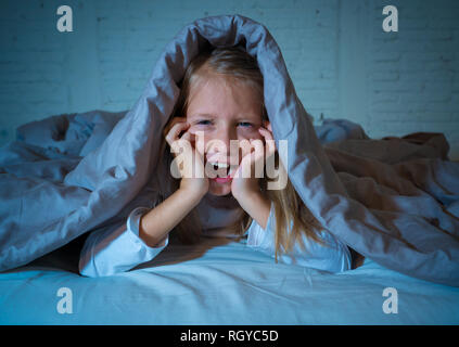 Carino addormentato ragazza urlando e piangendo dopo aver paura o ricalcatura sogno copertura lei stessa con coperta in letto a notte in mood illuminazione drammatica in Foto Stock