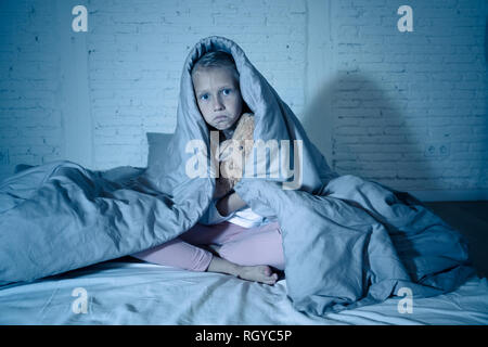 Carino addormentato ragazza urlando e piangendo dopo aver paura o ricalcatura sogno copertura lei stessa con coperta in letto a notte in mood illuminazione drammatica in Foto Stock