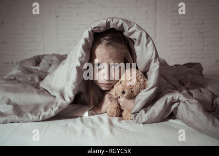 Carino addormentato ragazza urlando e piangendo dopo aver paura o ricalcatura sogno copertura lei stessa con coperta in letto a notte in mood illuminazione drammatica in Foto Stock