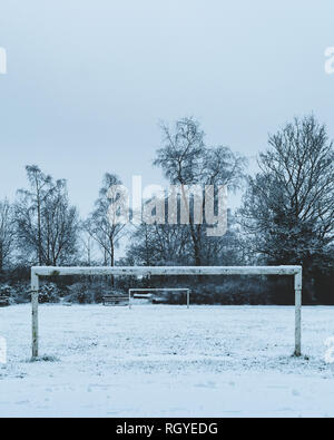 Un inverno di colpo di un piccolo campo da calcio attraverso i pali con il passo coperta da fitti bianco della neve Foto Stock