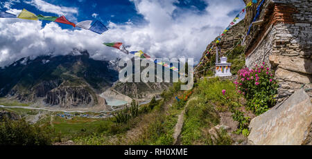 Antenna di panoramica vista sul villaggio e il gruppo di Annapurna in nuvole da Praken Gompa e colorati di preghiera buddista bandiere svolazzanti in aria Foto Stock