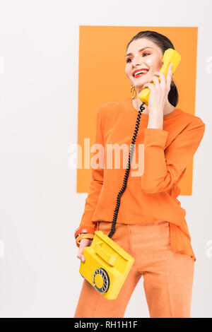 Moda Donna sorridente parlando al telefono retrò e posa con la curcuma sullo sfondo Foto Stock