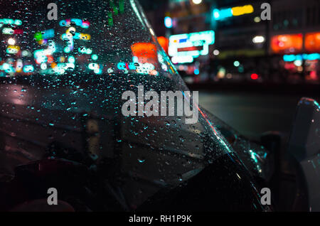 Abstract città notte sfondo sfocato, riflessi colorati e gocce di pioggia sul parabrezza bagnato Foto Stock