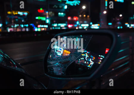 Abstract città notte sfondo sfocato, riflessi colorati e gocce di pioggia sul bagnato specchio auto Foto Stock