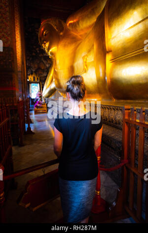 La donna guarda la statua dorata di Wat Phra Chetuphon Buddha sdraiato Bangkok in Thailandia Foto Stock