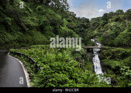 Strada di Hana: l'Autostrada Hana si trasforma per attraversare un ponte di corsia accanto a una cascata sulla costa nord di Maui. Foto Stock