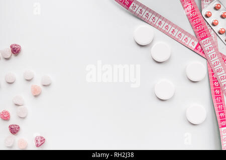 La perdita di peso e malsano concetto pericolose pillole su uno sfondo bianco con rosa candy Foto Stock