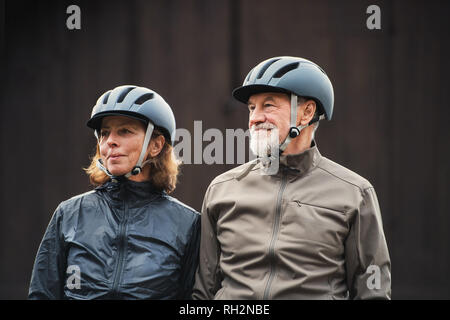 Attivo felice coppia senior con caschi moto in piedi all'aperto accanto all sfondo scuro. Foto Stock