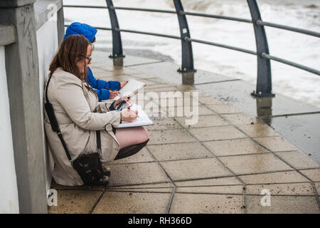 Due giovani studenti donne a Aberystwyth University School of Art oudoors disegno e delineando le onde causati dalla tempesta Diana Wales UK Foto Stock