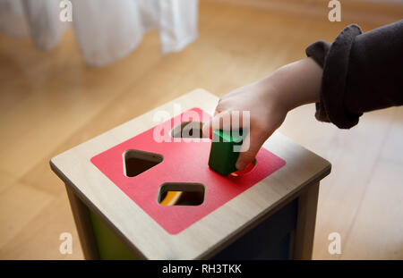 Bambini che giocano con mattoni di legno in diverse forme e colori cercando di inserirle nel foro corretto Foto Stock